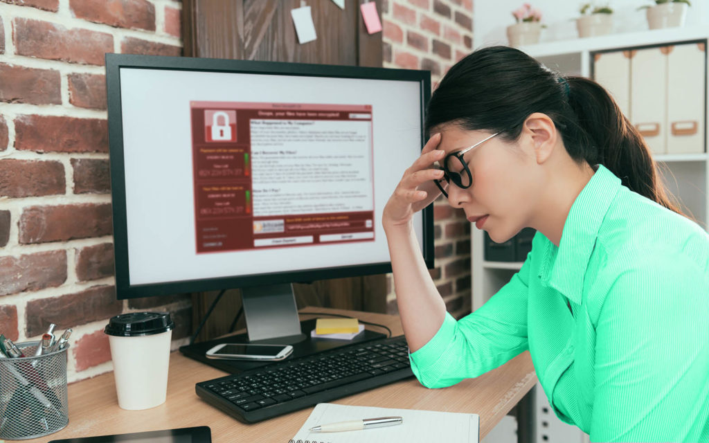 A photo of a woman holding her head in her hand when she realizes that her computer is infected with ransomware