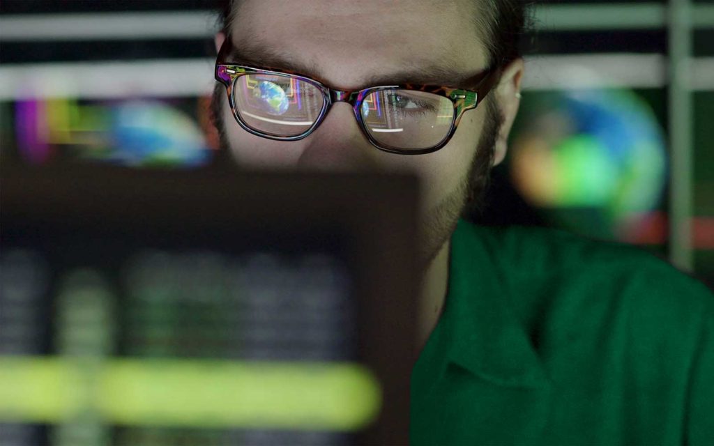 Digital forensics vs cyber security: A stock photo of a man looking at a screen that represents a cyber security expert analyzing security-related data